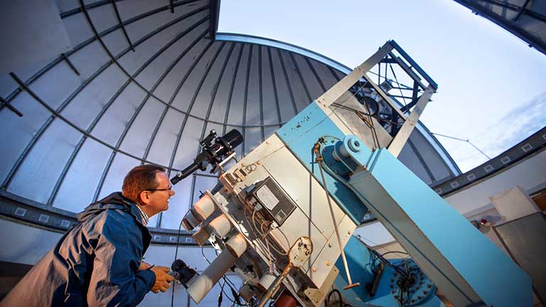 A man peers through a telescope at Fuertes Observatory