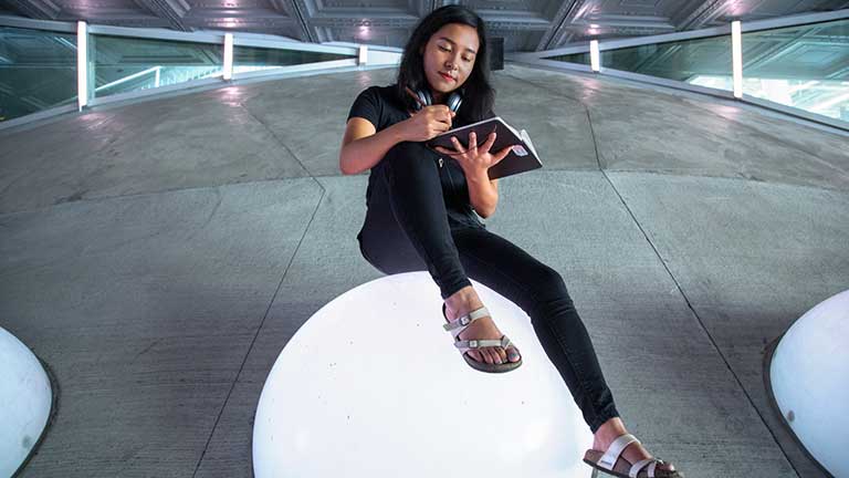 A student sitting atop a glowing sphere at Milstein Hall